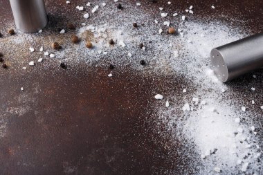 Tuz ve biberlikler devrildi ve içindekiler kahverengi bir masaya döküldü. İnce tuz ve bütün biberler mutfağın yüzeyini kaplar. Sahne yemek pişirirken oluşan karmaşayı gösteriyor..