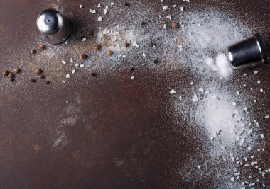 Tuz ve biber kapları kahverengi bir yüzeye düşmüş. Baharatlar tüm yüzeye yayılır, mutfakta kirli bir bölge olduğunu gösterir. Bu sahne yemek hazırlıkları sırasında meydana gelebilir..