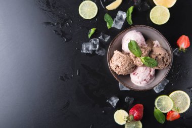 Bir kasede farklı tatlarda üç top dondurma bulunur. Kasenin etrafında taze çilekler, dilimlenmiş limonlar ve limonlar var. Buz ve nane yaprakları aranjmana eklenir.