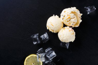 Üç kepçe limonlu dondurma karanlık bir yüzeye konur. Dondurmanın etrafında buz küpleri var ve yakınlarda bir dilim limon var. Sahne ferahlatıcı bir şey gösteriyor..