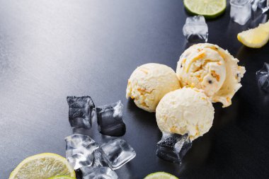 Üç kepçe dondurma siyah bir yüzeye oturur. Etraflarında buz küpleri ve limon dilimleri var. Taze ve davetkar görünüyor. Zevk almak için mükemmel..