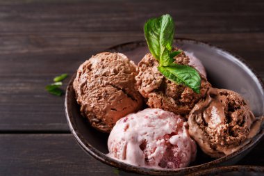 Dört kepçe dondurma bir kasede ahşap bir masada oturuyor. Tadı çikolata ve çilek içeriyor. Üzerine bir nane filizi konur..