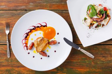 Sos ve küçük süslemelerle servis edilen bir tavuk tabağı beyaz bir tabakta salatanın yanında duruyor. Dekor ahşap bir masa gösteriyor. Masanın üzerine bir çatal ve bıçak yerleştirildi..