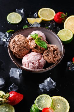 Bir kase taze çilek ve limon dilimlerinin yanında birkaç kepçe dondurma tutar. Buz küpleri siyah bir yüzey üzerinde kasenin etrafını sararak canlandırıcı bir manzara yaratıyor..