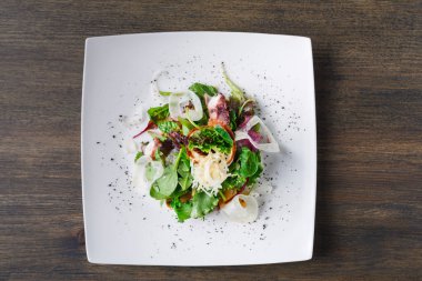 Bir tabakta çeşitli sebze ve sebzelerden yapılmış taze bir salata bulunur. Salatada marul, soğan ve hafif bir sos var. Tahta bir masaya konur..