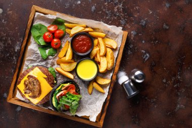 Tahta tepside köfte, marul ve domatesli bir çizburger var. Ayrıca altın kızartmalar, kiraz domatesleri ve iki soslu kase var. Bu yemek tadını çıkarmaya hazır..