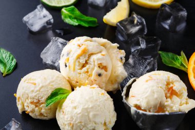 Karanlık bir yüzeye üç kepçe dondurma konur. Limon, limon ve portakal dilimlerinin yanında oturuyorlar. Buz küpleri ve nane yaprakları kepçelerin etrafına saçılmış..