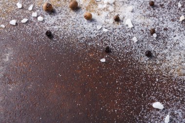 Tuz ve biber koyu, kırsal bir yüzeye saçılmıştır. Tahıllar düzensiz dağılımla basit bir şablon oluşturuyor. Mutfak havası veriyor ve yemeklerde kullanılmaya hazır baharatları gösteriyor..