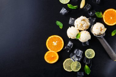 Dondurma kepçeleri taze portakal ve limon dilimleri ile çevrili karanlık bir yüzeyde otururlar. Buz küpleri ve nane yaprakları renk ve tazelik ekler. Sahnede bir kepçe aracı da görünür.