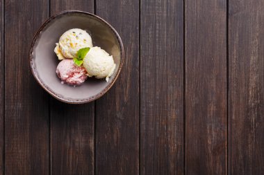 Üç farklı kepçe dondurma ahşap bir masada bir kasede duruyor. Ayarlar basit ve gündüz vaktidir. Ekranda çeşitli tatlar ve dekorasyon olarak bir nane yaprağı yer alıyor..