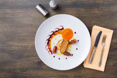 Bir tabak tavuğu yumurtayla servis eder, üzerine sos serpiştirilir ve küçük detaylarla süslenir. Bir çatal ve bıçak, tabağın yanında, tahta bir masanın üzerinde peçeteyle oturuyor..