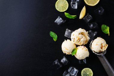 Siyah bir yüzeye üç kepçe dondurma konur. Yakınlarda limon dilimleri, nane yaprakları ve buz küpleri var. Sahne, sıcak hava için ferahlatıcı bir tatlı düzenini gösteriyor..