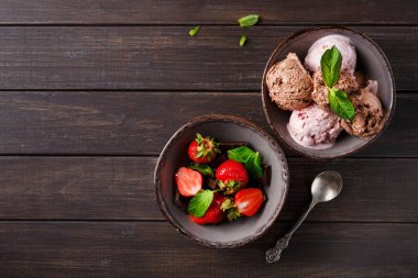 Tahta bir masanın üzerine iki kase konur. Bir kasede çeşitli dondurma kepçeleri, diğerinde ise nane yapraklı taze çilekler var. Kâselerin yanında bir kaşık yatıyor..