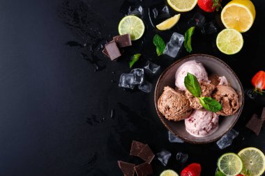 Dondurma kepçeleri, etrafı dilimlenmiş meyve ve çikolata parçalarıyla çevrili bir kasede oturur. Taze nane yaprakları renk katar. Sahnede erimiş buz var..