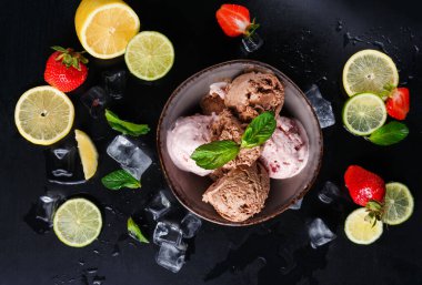 Farklı aromalı dondurma bir kaseye konur. Limon dilimleri ve limon kasenin etrafını çilek ve buzla çevreler. Ayar karanlık bir yüzeye sahip..