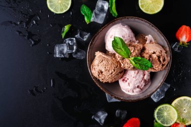 Bir kâse karanlık bir yüzeye yerleştirilmiş üç çeşit dondurma içerir. Kasenin etrafında limon dilimleri, çilekler ve buz küpleri var. Taze nane yaprakları biraz renk katar..