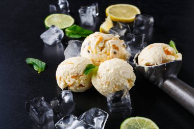 Üç kepçe dondurma, etrafı buz küpleriyle çevrili karanlık bir yüzeyde oturur. Yakınlarda limon dilimleri ve nane yaprakları var. Kurulum davetkar ve taze, bir yaz ziyafeti öneriyor..