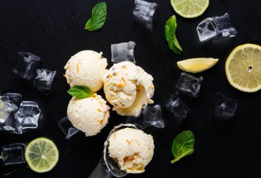 Dört kepçe limonlu dondurma, buz küpleri, nane yaprakları ve siyah bir yüzeyde limon dilimleri ile düzenlenir. Sıcak bir günde tatlının tadını çıkarmaya hazırız..