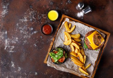 Tahta tepside peynirli bir hamburger ve yanında da marul-domates salatası var. Altın kızartmalar hamburgerin yanına oturur. Soslar tepsinin etrafına konur..