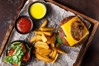 Peynirli ve soslu bir hamburger kızarmış patates dilimlerinin yanında oturur. Tepsiye taze malzemelerin yanına iki kase sos konur..
