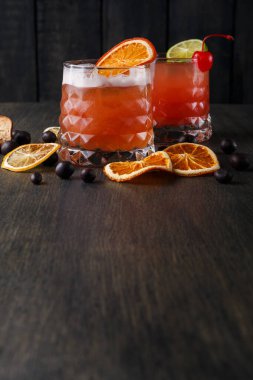 İki içki, her biri portakal dilimleri ve kirazla süslenmiş koyu ahşap bir masada oturur. Kurutulmuş portakal dilimleri ve koyu böğürtlenler bardakların etrafında.