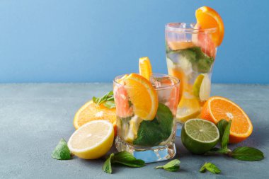 İçkiyle dolu iki bardak masaya oturur. İçeceklerde portakal, limon ve limon dilimleri var. Taze nane yaprakları da görülebilir. Arka plan mavi ve basit..