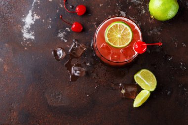 Kiraz ve kireçle yapılmış bir kokteyl köy masasında duruyor. İçkiye taze limon dilimleri ve kirazlar eşlik ediyor. Bazı buz küpleri camın etrafına saçılmış..