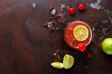 Bir içecek, buz küpleri ve limon dilimleriyle karanlık bir yüzeye oturur. Kırmızı kirazlar yakına konur. Bu ortam bir araya gelmek ya da rahatlamak için mükemmel olabilir..