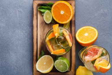 Soğuk narenciye içecekleriyle dolu iki bardak ahşap tepside oturur. İçkiler portakal, limon ve limonla süslenmiş. Taze nane yaprakları olay yerine renk katar.