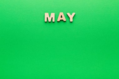 May kelimesi, saf yeşil arka planda tahta harfler kullanılarak düzenlenir. Harfleri net bir şekilde öne çıkaran parlak ve tekdüze bir renk içeren metne odaklanıyoruz..