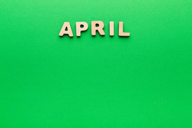 Sahne parlak yeşil bir arka planda sıralanmış ahşap harfleri gösteriyor. Harfler April kelimesini heceliyor. Bu ayar bahar ayını temsil ediyor..