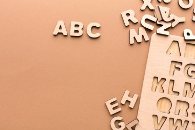 Tahta harfler açık kahverengi bir yüzey boyunca yayılır. Bazı harfler düzgünce bir tahtaya yerleştirilirken diğerleri etrafa saçılmış. Bu ayar çocuklara mektup öğretmek için uygundur.