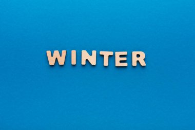 Ahşap harfler parlak mavi arka planda kış kelimesini heceler. Harfler ortalanmış ve okunması kolay. Bu sahne kış mevsimini ve karakteristik özelliklerini temsil ediyor..