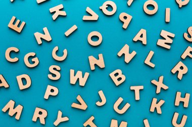 Alfabenin ahşap harfleri mavi arka plana dağılmış. Eğitici faaliyetler için kullanılırlar. Harfler çocukların öğrenmesi için çeşitli oyunlarda kullanılabilir..