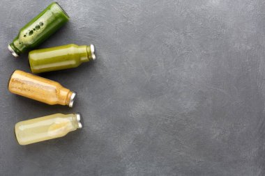 Gri bir yüzeye dört şişe taze meyve suyu konur. Meyve suları farklı renklerde ve sağlıklı görünüyor. Her şişenin metal bir kapağı var ve ağzına kadar dolu..