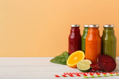 Dört şişe meyve suyu hafif bir yüzeye yerleştirilir. Yeşil bir yaprak, portakal ve limon dilimlerinin yanında renkli meyve suları bulunur. Çizgili pipetler de masada..