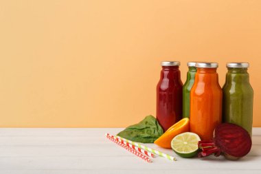 Dört şişe bir masada farklı sıvılar içerir. Taze meyve ve sebzeler yakınlarda bulunur. Renkli pipetler şişelerin yanına konur. Arka plan sıcak tonlarda..