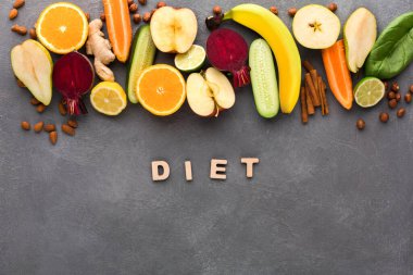 Renkli meyve ve sebzeler gri bir yüzeye yerleştirilir. Diyet kelimesi ortada ahşap harflerle yazılır. Bu kurulum çeşitli sağlıklı yiyecek seçeneklerini gösterir.