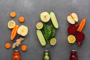 Taze meyve ve sebzeler üç grup halinde düzenlenir. Havuç, salatalık, elma ve daha fazlası görülebilir. Meyve suyu şişeleri gri bir yüzeyin altına yerleştirilir..