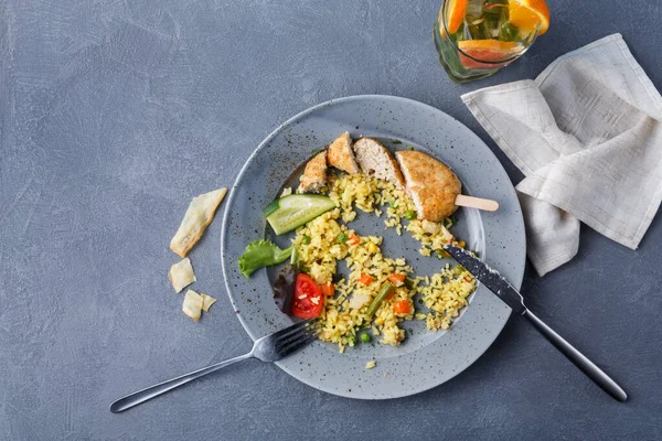 Tabakta bir öğün pirinç, sebze ve tavuk kalıntıları var. Meyveli bir içecek yakınlarda durur. Mekan sıradan bir atmosferi olan basit bir yemek alanı..