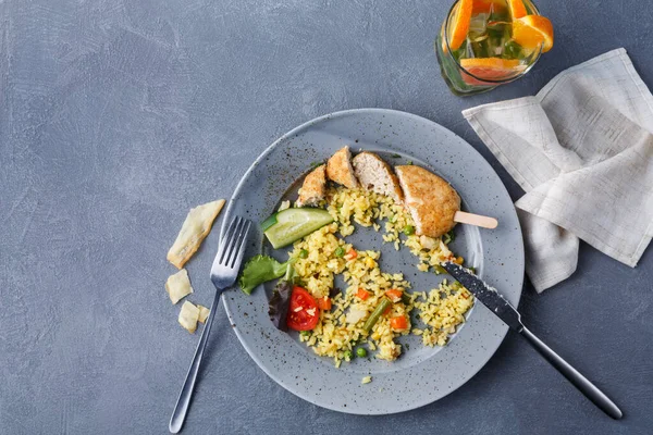 Bir tabakta sebze ve tavuk parçalarıyla karışık pirinç var. Çatal ve bıçak tabağın yanına oturur. Yakınlarda renkli bir içecekle bir bardak gösteriliyor. Masada biraz yemek var..