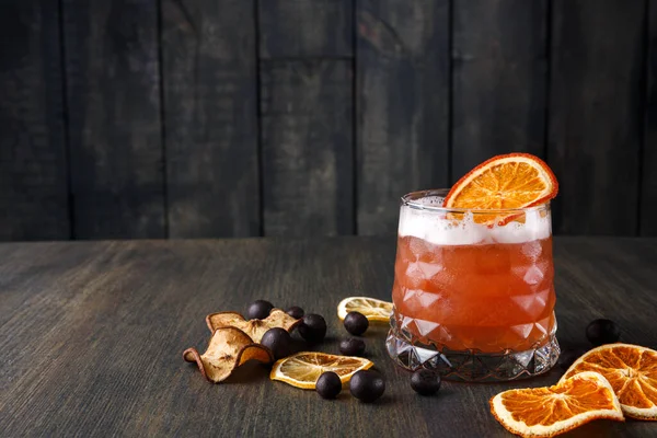 Kurutulmuş portakal dilimleri ve koyu böğürtlenlerle dolu ahşap bir masada bir içki duruyor. Ortam sıcak ve davetkar görünüyor, ferahlatıcı bir içeceğin tadını çıkarmak için mükemmel..