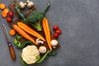 Taze sebzeler ahşap kesme tahtasına konur. Havuç, brokoli, karnabahar, domates ve mantarlar düzgünce düzenlenmiştir. Yakınlarda bir bıçak var, kesmeye hazır..