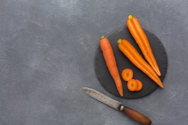Bazı taze havuçlar siyah bir tabağa konur. Havuçların yanında bir bıçak var. Ayar gri bir yüzeyde. Saat sabahın geç saatleri, doğal ışıkla.