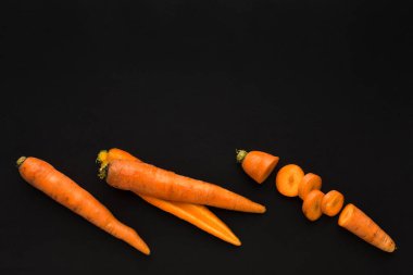 Siyah bir yüzeye serilmiş havuçlar bütün havuçları ve bazı kesikleri yuvarlak parçalara ayırır. Bu ayar akşam ışığında sebzelerin doğal şeklini ve rengini gösterir.