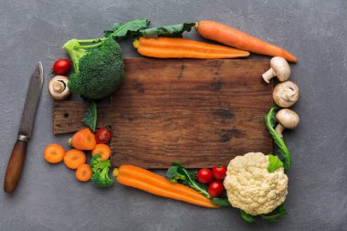 Taze sebzeler mutfak ortamındaki ahşap bir kesme tahtasının etrafına konur. Havuç, brokoli, karnabahar ve mantar kullanıma hazır bir bıçakla birlikte görülebilir..