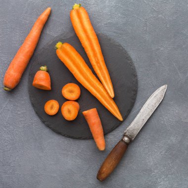 Birkaç taze havuç siyah bir tahta üzerine yerleştirilir. Bazı havuçlar bütündür, diğerleri ise parçalara ayrılmıştır. Havuçların yanında bir bıçak duruyor. Sahne parlak ve basit..