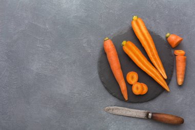 Farklı boyutlarda havuçlar siyah bir tabağa konur. Yanlarına bir bıçak konur. Ayarlar basit ve sebzelerin yemek pişirmeye hazırlanmasına odaklı..