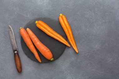 Birkaç taze havuç koyu yuvarlak bir yüzeye bir mutfak bıçağının yanına yerleştirilir. Sahne yemek hazırlığı ya da mutfakta yemek tarifi aktivitesi öneriyor..