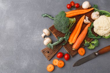 Tahta kesme tahtasına havuç, brokoli, karnabahar ve mantar da dahil olmak üzere taze sebzeler yerleştirilir. Yanlarına bir bıçak yerleştirilir. Renkli kiraz domatesleri sahneye ekleniyor.